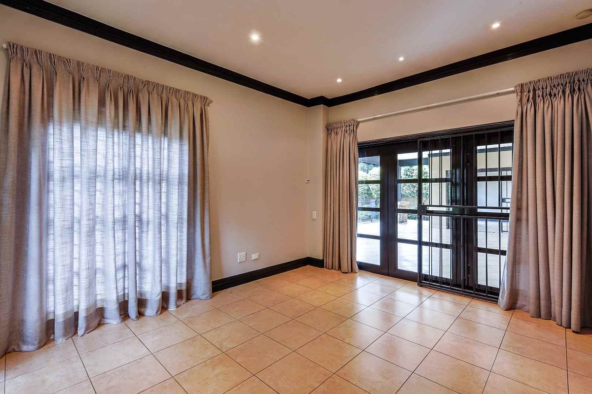 A spacious, empty living room featuring tiled flooring, dark crown molding, recessed lighting, and double glass doors leading to an outdoor area.