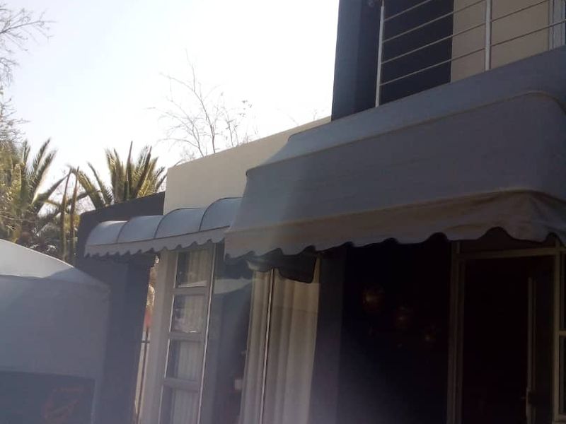 Front elevation of the apartment building featuring a balcony with metal railings, aluminium window frames, and a fabric awning over the ground floor entrance.