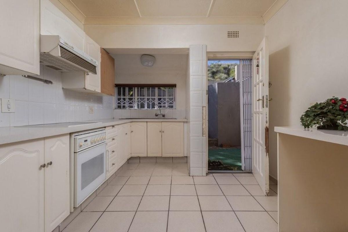 A dated kitchen featuring white cabinetry, a built-in oven and extractor fan, tiled flooring, and direct access to an outdoor area.