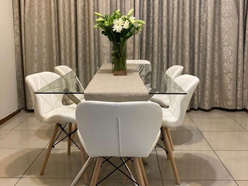 A well-lit dining area featuring neutral tiled flooring and full-length floor-to-ceiling curtains.