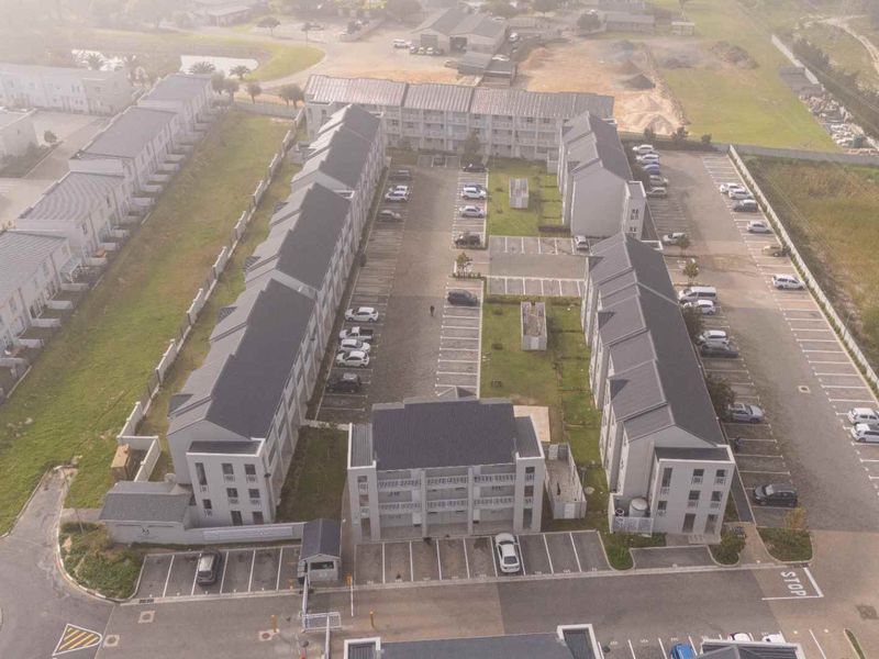 Aerial view of a modern apartment complex featuring multiple residential blocks, dedicated parking bays, and secure gated access.