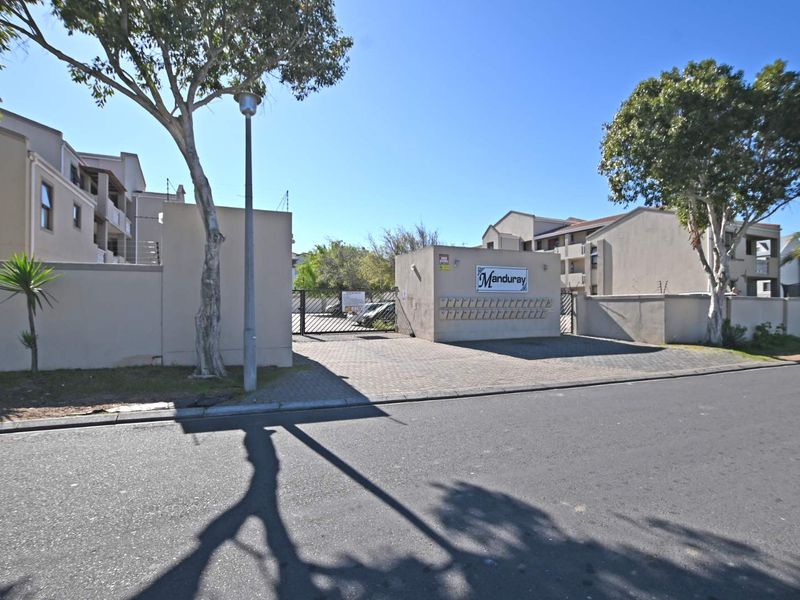Front entrance view of the Manduray apartment complex featuring a paved driveway, secure gated access, and exterior post boxes.