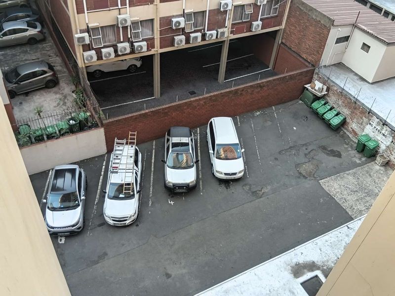 An elevated aerial view of an apartment complex parking area featuring asphalt bays, brick boundary walls, and external air conditioning units.
