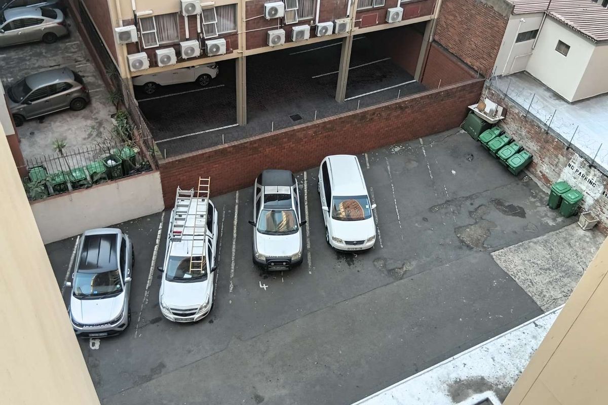 An elevated aerial view of an apartment complex parking area featuring asphalt bays, brick boundary walls, and external air conditioning units.