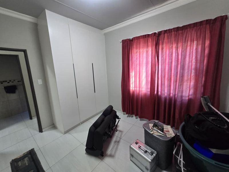 A bedroom featuring white built-in wardrobes, neutral tiled flooring, and decorative ceiling cornicing.