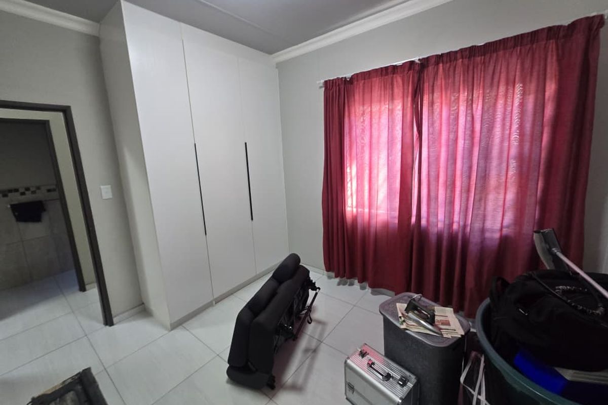 A bedroom featuring white built-in wardrobes, neutral tiled flooring, and decorative ceiling cornicing.