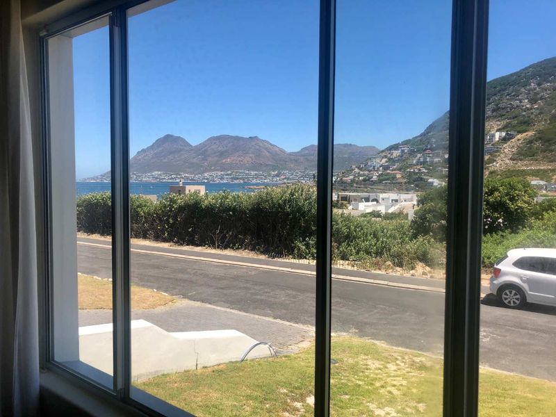 A clear view of the ocean, mountains, and surrounding neighborhood captured through a large window.