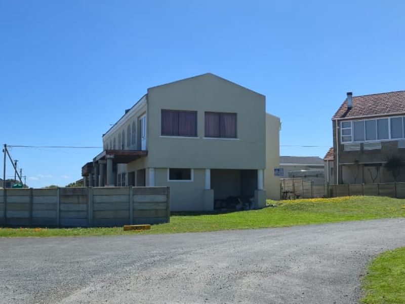 A view of the property exterior featuring a multi-level building with a tiled roof, concrete boundary wall, and gravel driveway access.