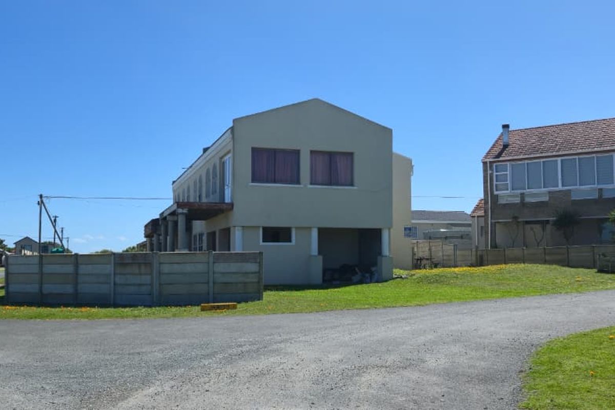 A view of the property exterior featuring a multi-level building with a tiled roof, concrete boundary wall, and gravel driveway access.