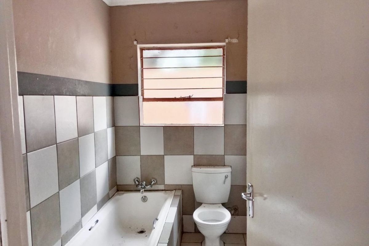 A dated bathroom featuring a standard bathtub, toilet, and tiled walls with a window providing natural light.