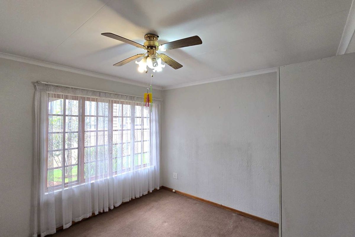 A bright, empty bedroom featuring a ceiling fan, built-in cupboard, and large window with natural light, ready for personalization.