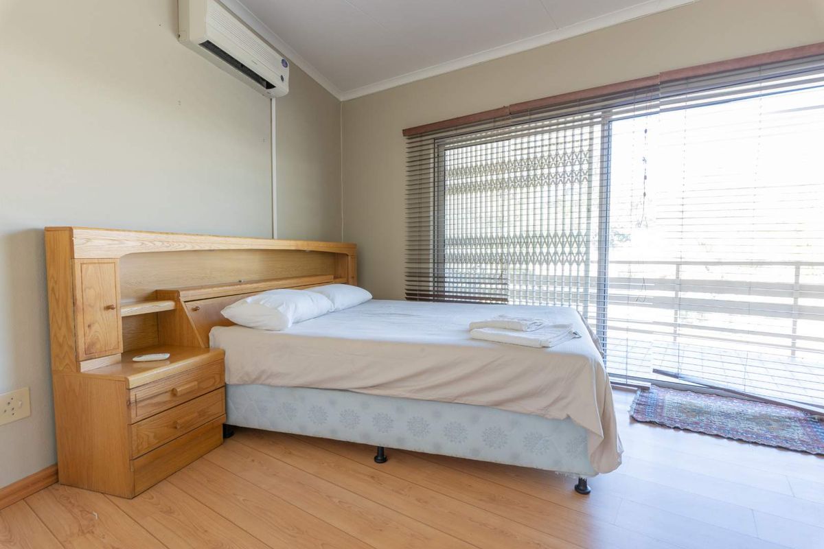 A bedroom featuring laminate flooring, a wall-mounted air conditioning unit, and a sliding glass door with venetian blinds providing access to the exterior.