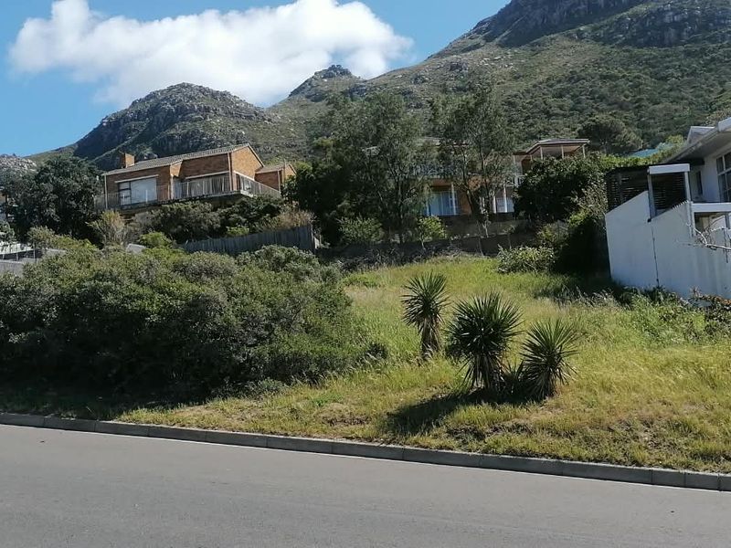 A sloped vacant residential plot situated in a developed neighborhood with mountain views and established road access.