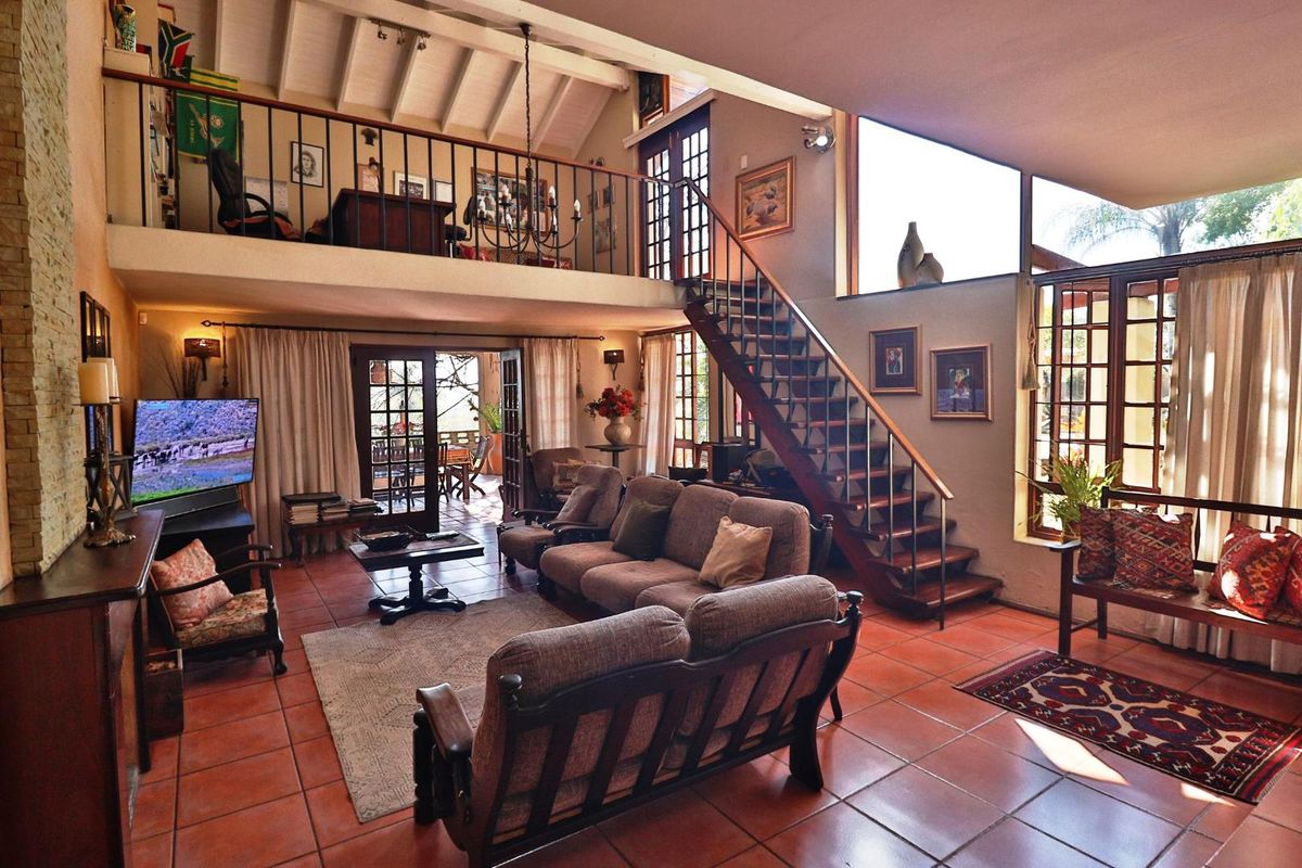 Spacious double-volume living area featuring terracotta flooring, exposed timber beams, a mezzanine level, and large windows providing abundant natural light.