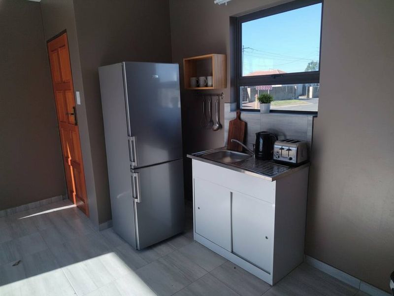 A compact kitchen area featuring a stainless steel sink, tiled splashback, and tiled flooring, with a timber door and aluminium window frame.