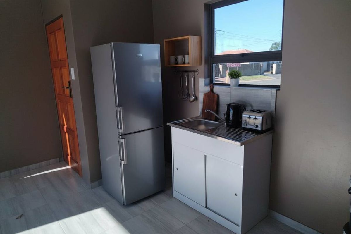 A compact kitchen area featuring a stainless steel sink, tiled splashback, and tiled flooring, with a timber door and aluminium window frame.