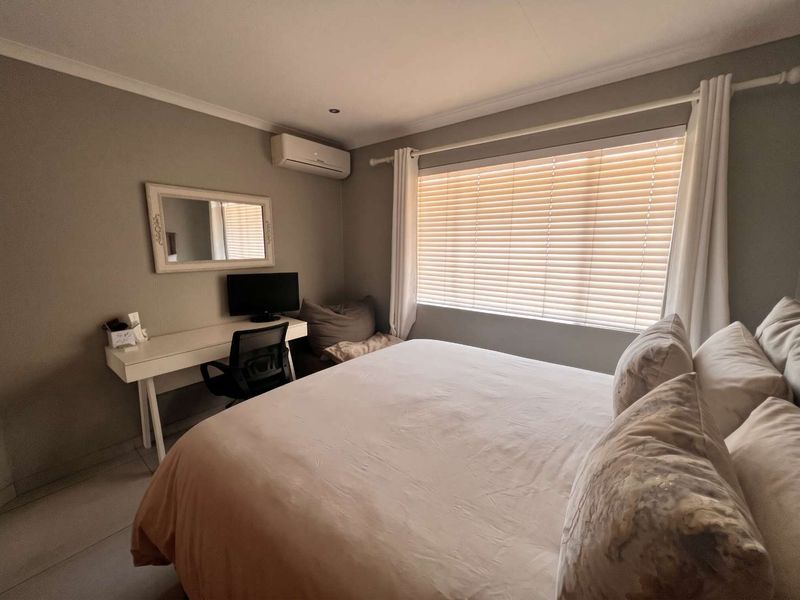 A well-maintained bedroom featuring tiled flooring, an integrated air conditioning unit, and venetian blinds for adjustable natural light.