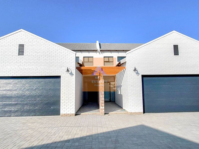 Front elevation of a modern townhouse featuring a paved driveway, double garages, and a timber pergola entrance.