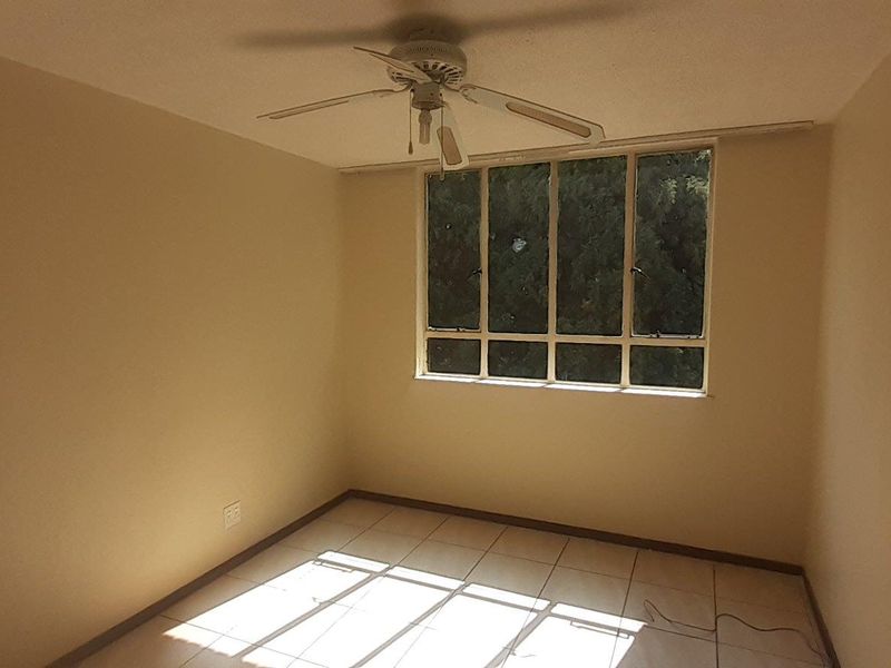 A vacant bedroom featuring neutral walls, tiled flooring, and a ceiling fan, offering a blank canvas for personalization.