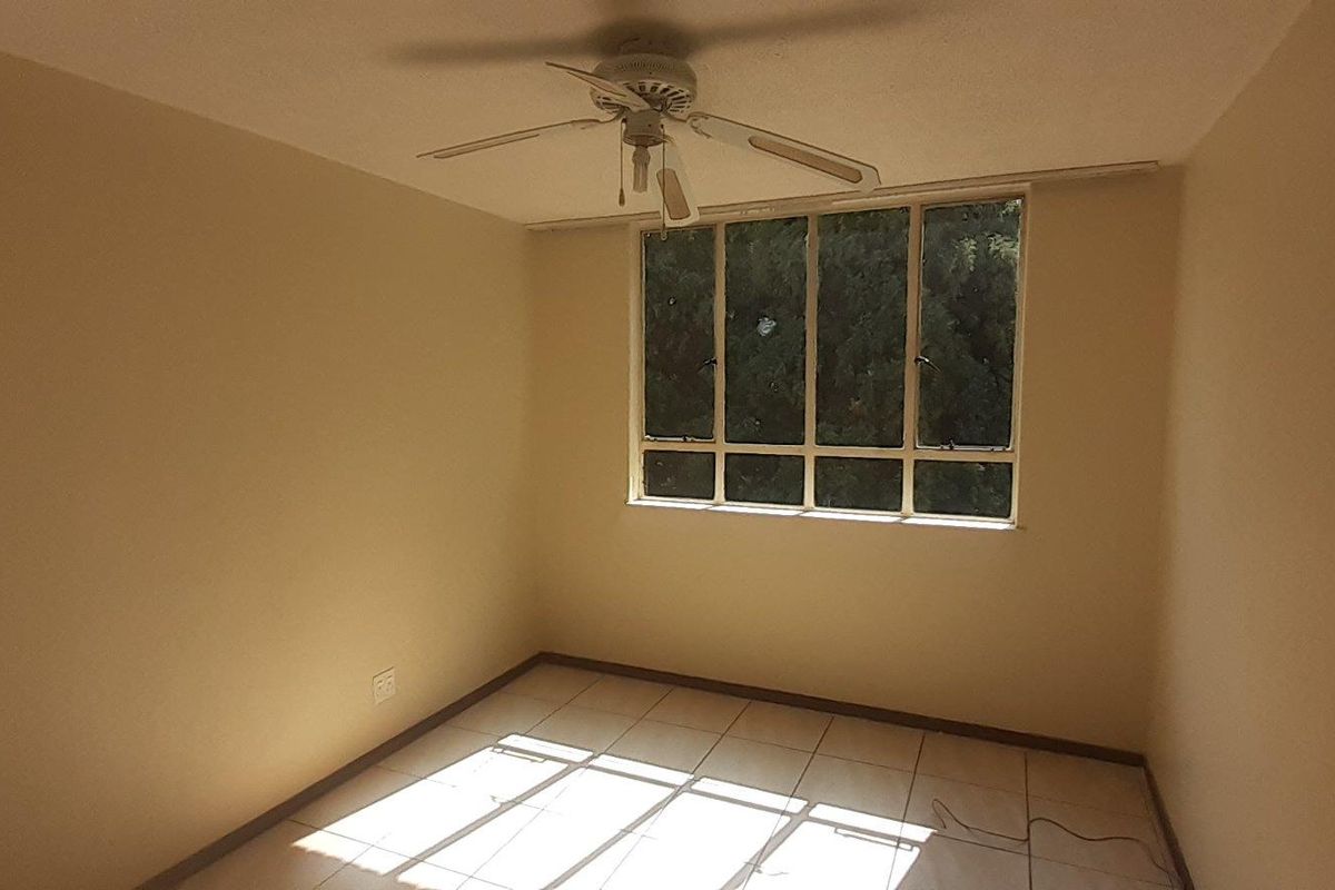A vacant bedroom featuring neutral walls, tiled flooring, and a ceiling fan, offering a blank canvas for personalization.
