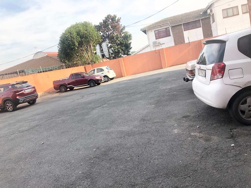An outdoor parking area featuring an asphalt driveway enclosed by a perimeter wall with security fencing.