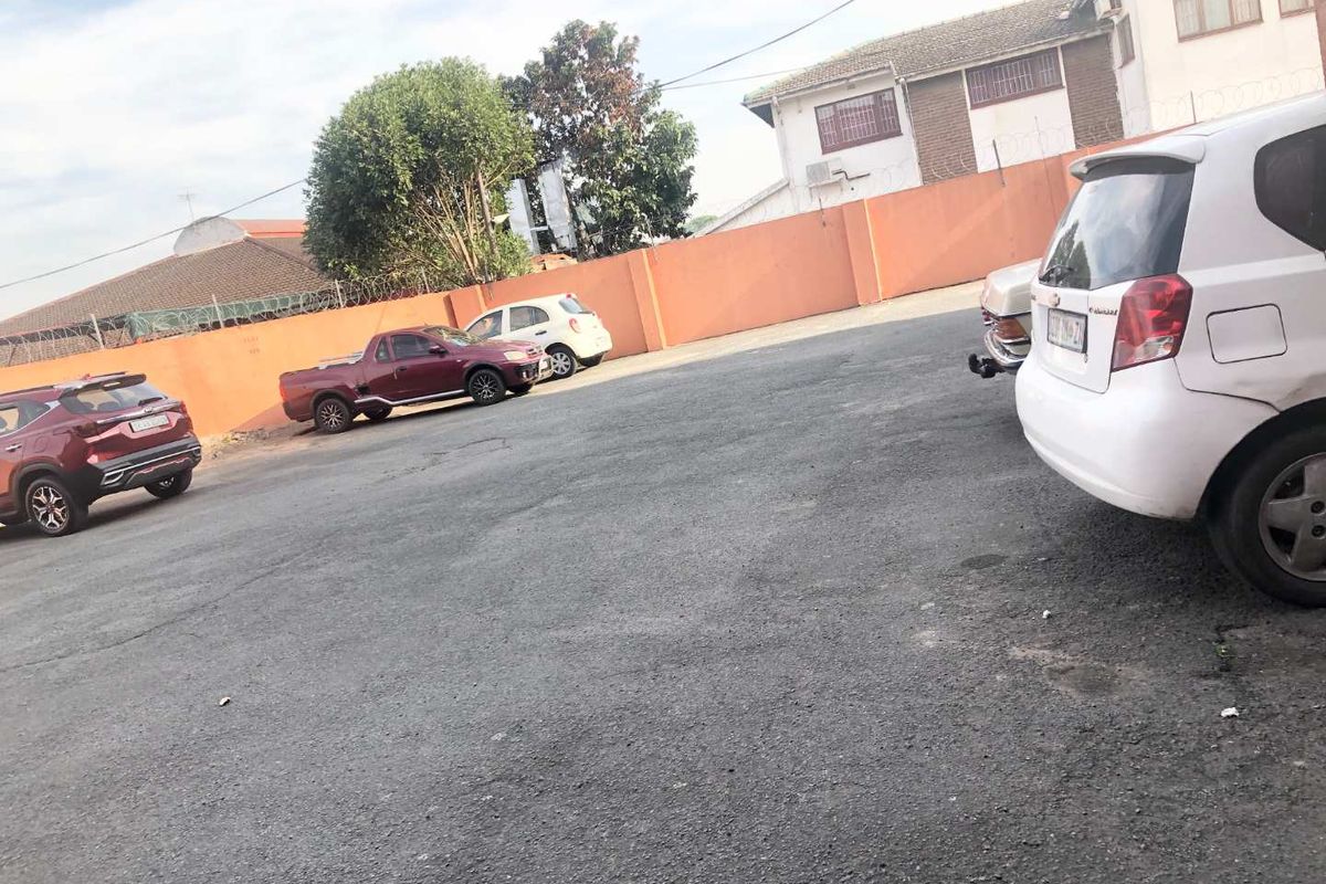 An outdoor parking area featuring an asphalt driveway enclosed by a perimeter wall with security fencing.