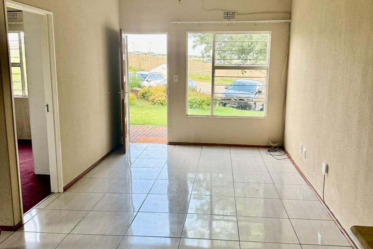 An empty living area featuring tiled flooring, a raked ceiling, and direct access to an outdoor garden space through a side door.