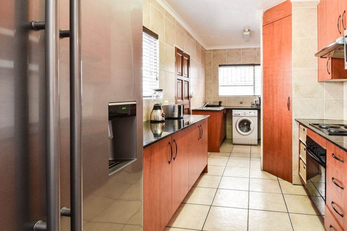 A functional kitchen featuring wood-finish cabinetry, granite countertops, tiled flooring, and integrated laundry facilities, offering a practical layout for daily meal preparation.