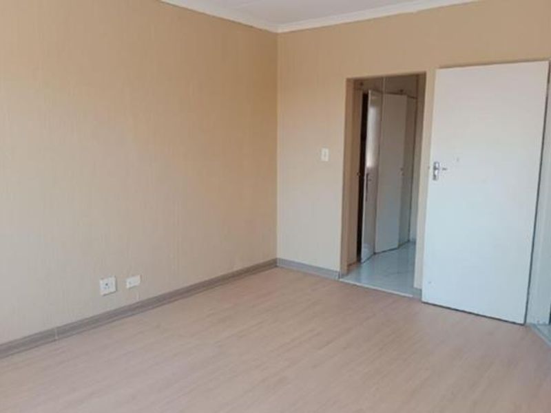 A clean, empty bedroom featuring light-toned laminate flooring, neutral walls, and a built-in cupboard, offering a blank canvas for personalization.