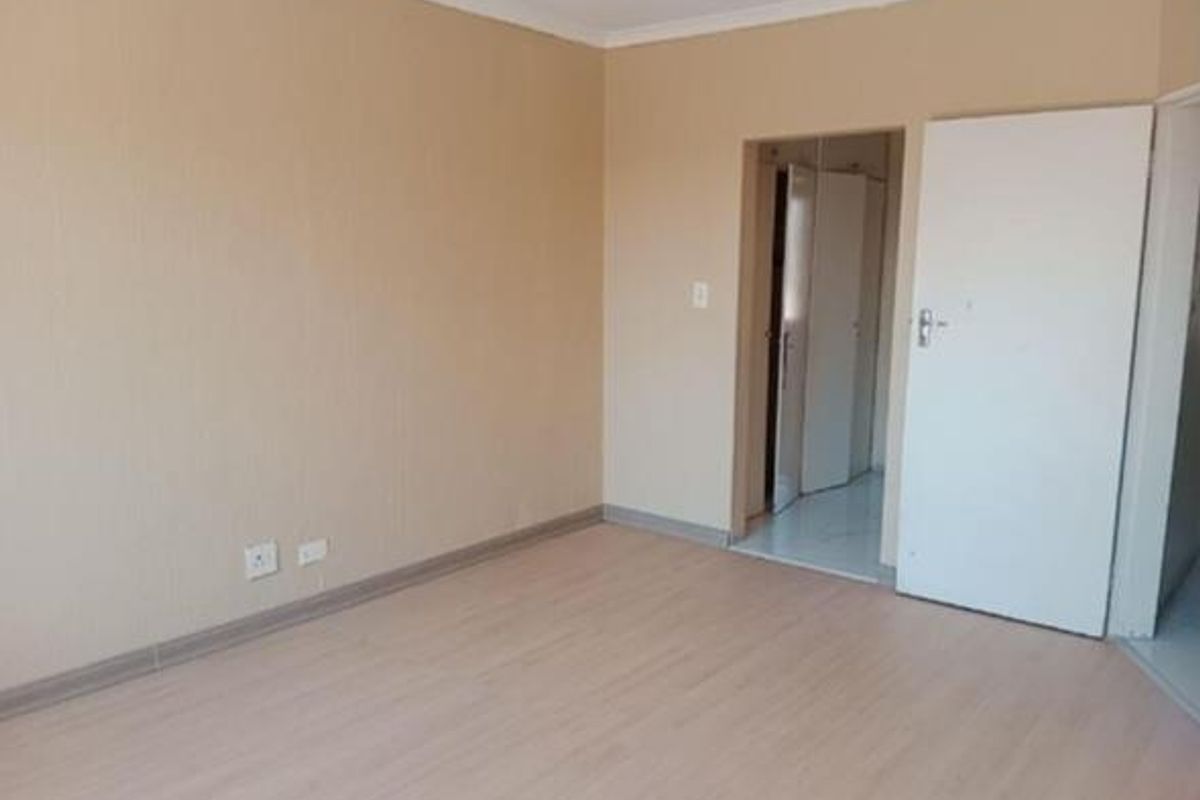 A clean, empty bedroom featuring light-toned laminate flooring, neutral walls, and a built-in cupboard, offering a blank canvas for personalization.