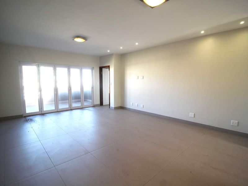 A spacious, empty living area featuring large sliding glass doors, neutral tiled flooring, and modern recessed lighting throughout.
