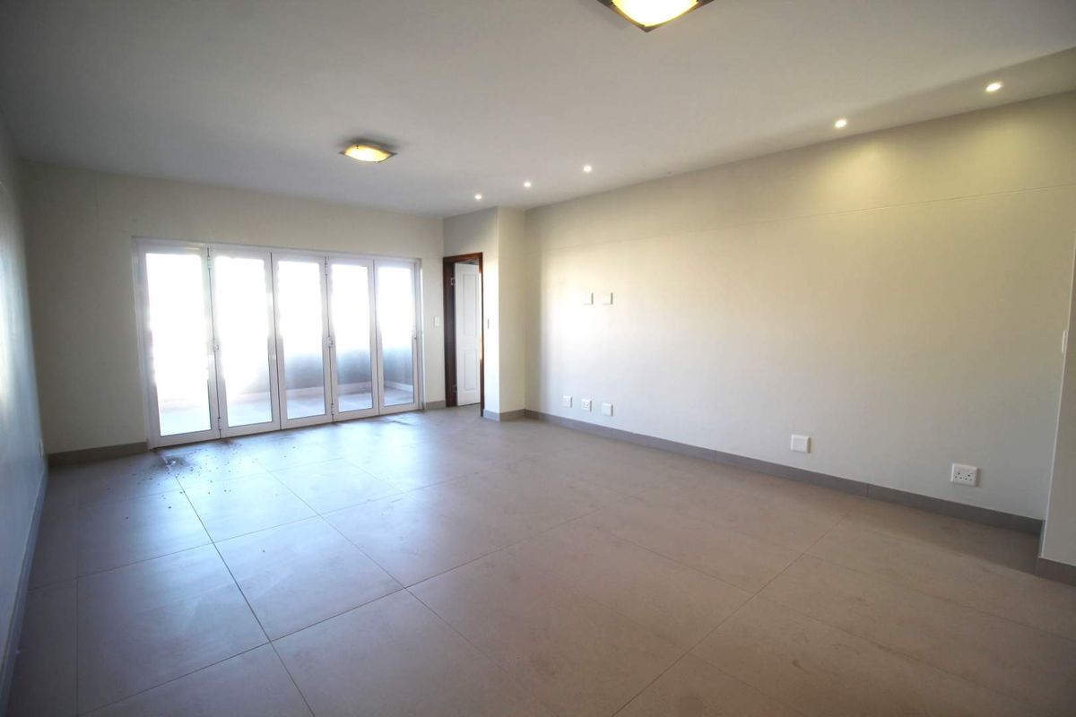 A spacious, empty living area featuring large sliding glass doors, neutral tiled flooring, and modern recessed lighting throughout.