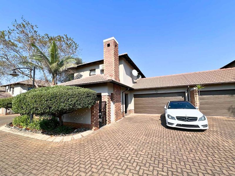 Front exterior view of a townhouse featuring a paved driveway, double garage, and a prominent brick chimney.