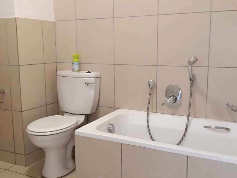 A functional bathroom featuring a standard bathtub with a shower mixer and a toilet, finished with neutral wall and floor tiles.