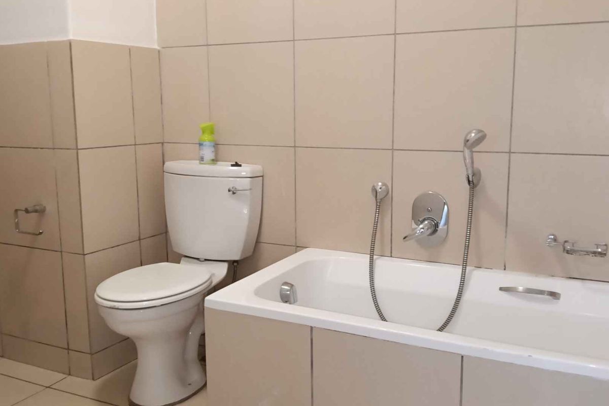 A functional bathroom featuring a standard bathtub with a shower mixer and a toilet, finished with neutral wall and floor tiles.
