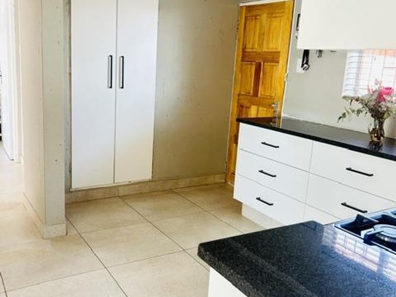 A functional kitchen space featuring white cabinetry, dark granite countertops, a gas hob, and neutral floor tiles, ready for final finishing touches.