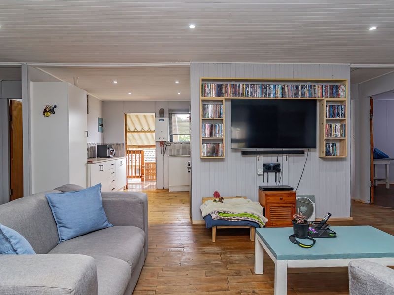 Open plan living area featuring timber flooring, recessed lighting, and a built-in media shelving unit, flowing into a functional kitchen space.