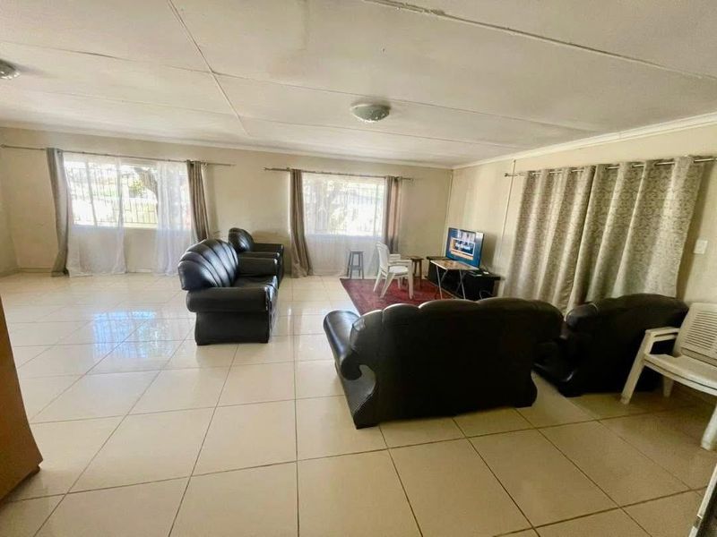 Spacious living area featuring large windows, neutral tiled flooring, and a drop-ceiling design, offering a bright and open layout.