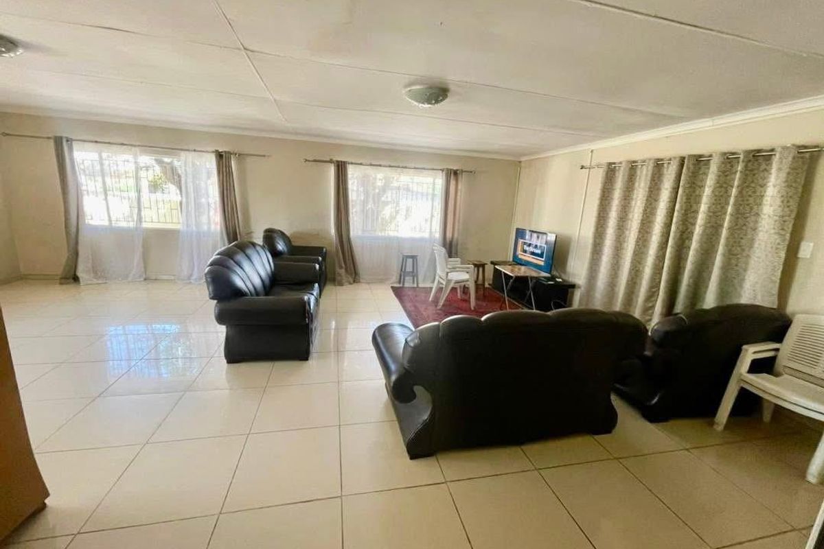 Spacious living area featuring large windows, neutral tiled flooring, and a drop-ceiling design, offering a bright and open layout.
