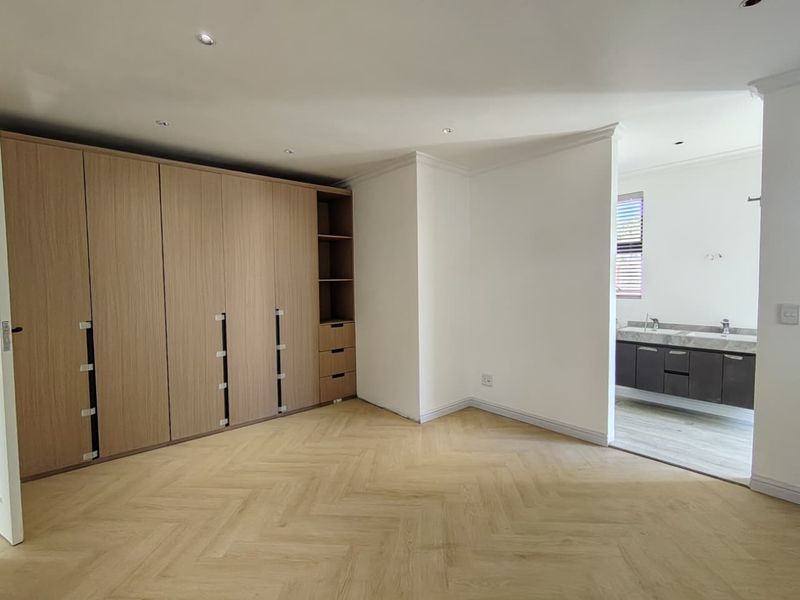 Spacious bedroom featuring modern herringbone flooring, extensive built-in cabinetry, and an open-plan en-suite bathroom with a contemporary vanity.