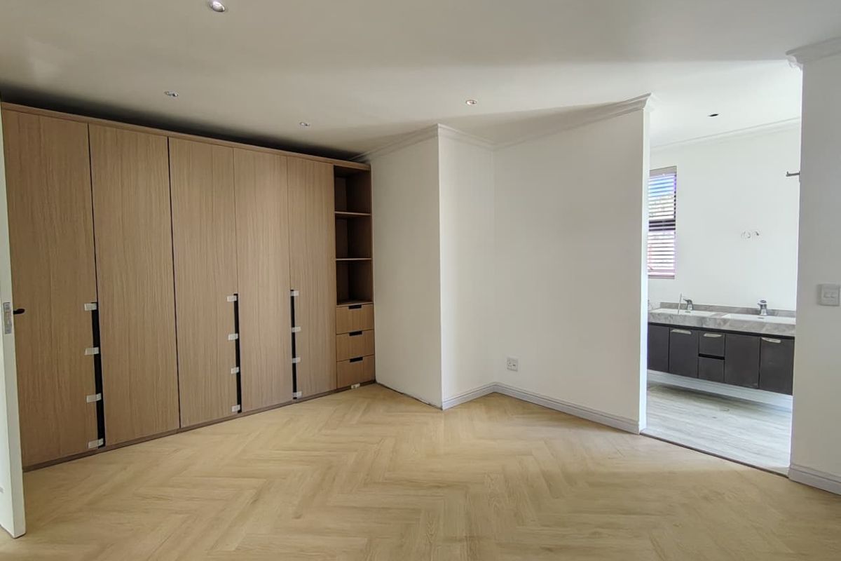 Spacious bedroom featuring modern herringbone flooring, extensive built-in cabinetry, and an open-plan en-suite bathroom with a contemporary vanity.