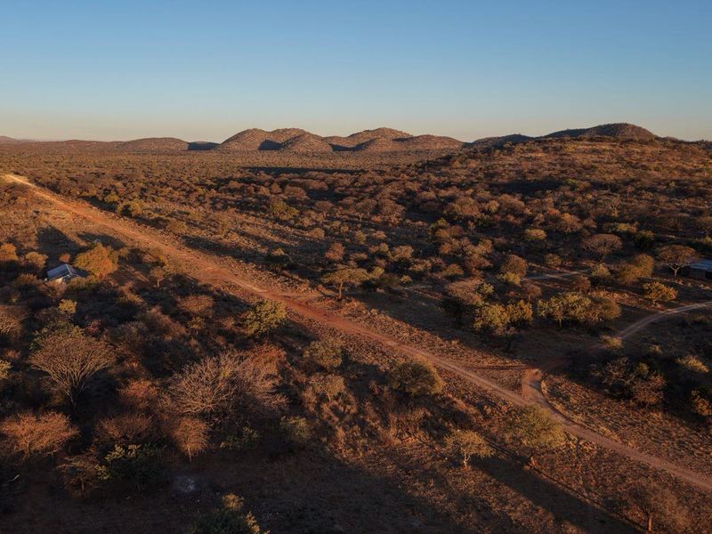 An aerial view of the expansive lodge property, showcasing the natural landscape, surrounding hills, and the access road leading to the structures.