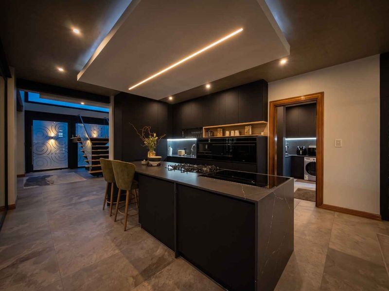 Modern, high-end kitchen featuring a large central island with stone countertops, integrated appliances, sleek dark cabinetry, and sophisticated recessed lighting.