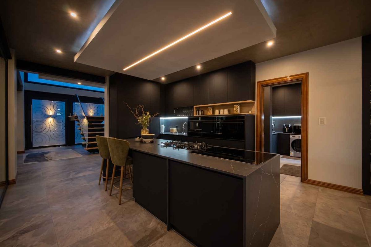 Modern, high-end kitchen featuring a large central island with stone countertops, integrated appliances, sleek dark cabinetry, and sophisticated recessed lighting.