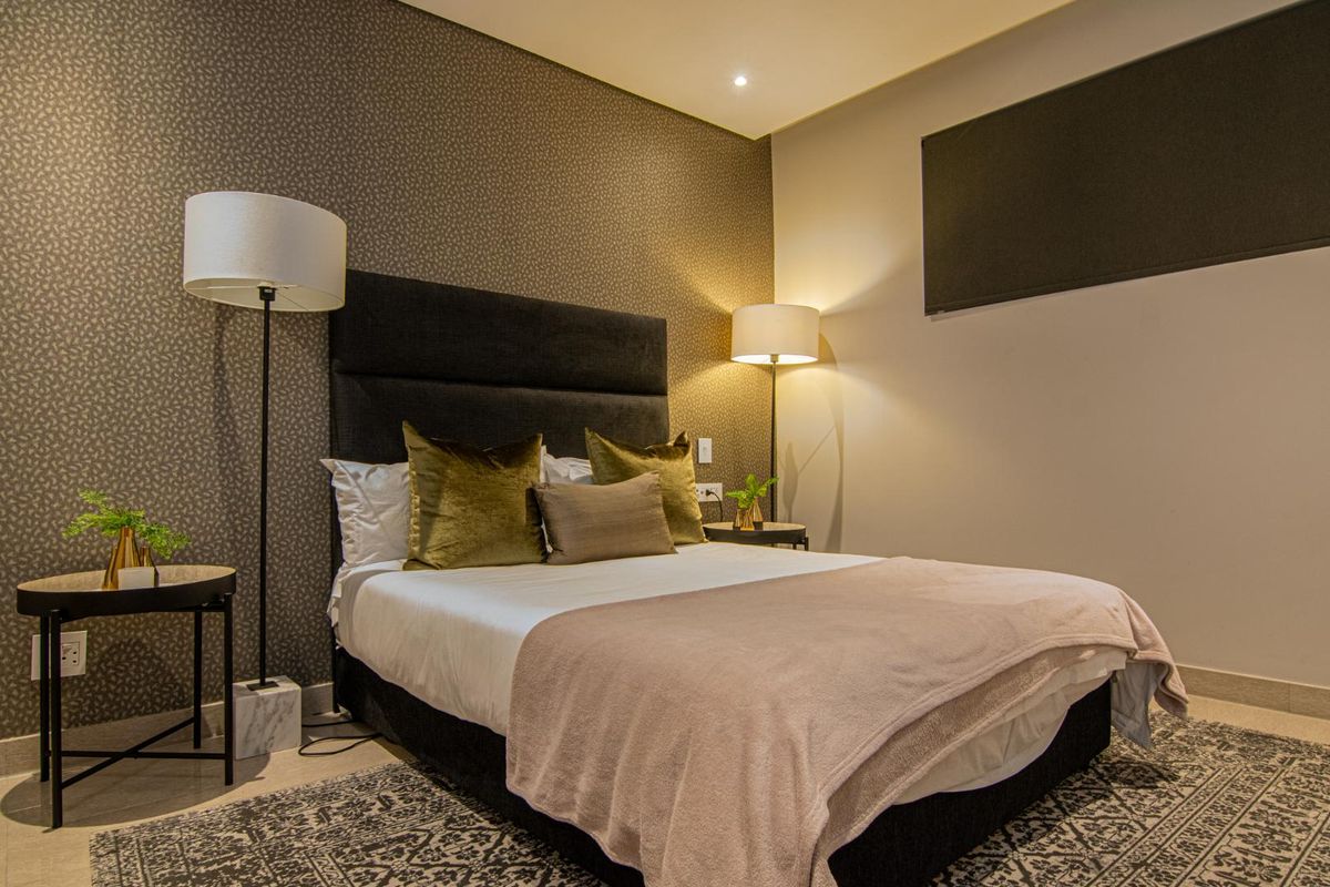 A well-appointed bedroom featuring a textured accent wall, recessed ceiling lighting, and neutral tiled flooring.