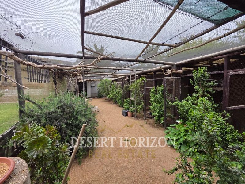 Outdoor garden area featuring a large timber-framed structure with shade netting and multiple wire mesh enclosures, suitable for an aviary or specialized animal housing.