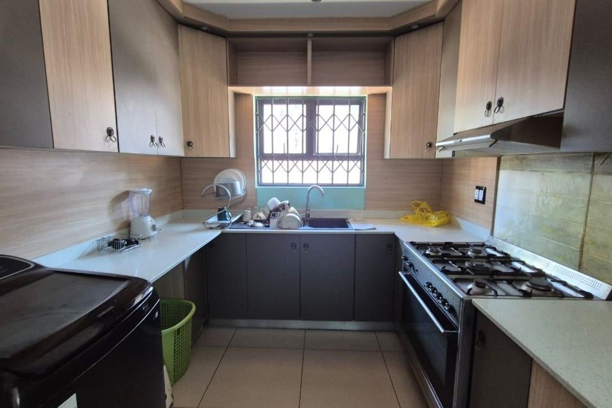 Functional kitchen featuring laminate cabinetry, built-in gas hob, oven, extractor fan, and a window with security bars.