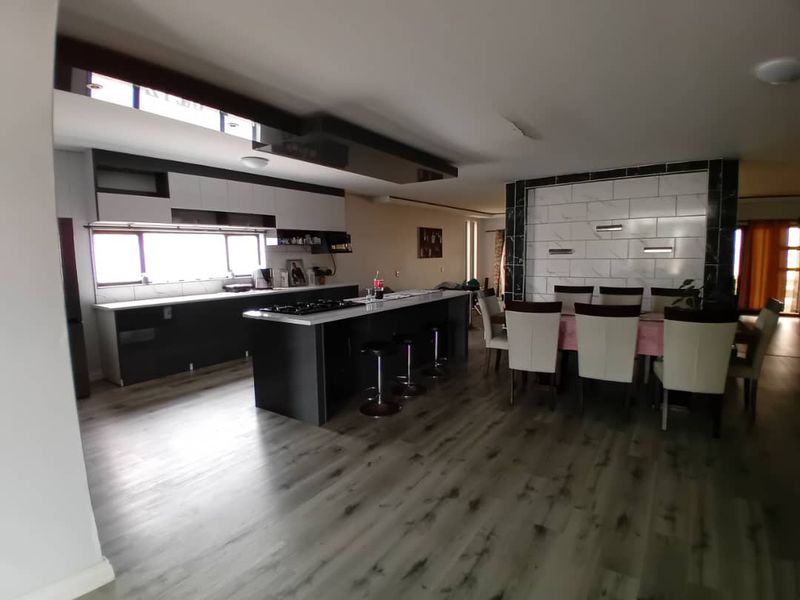 Spacious open-plan kitchen and dining area featuring a modern kitchen island with built-in hob, sleek cabinetry, and contemporary laminate flooring throughout.