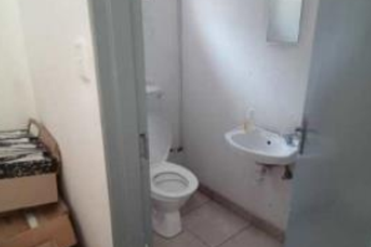 A compact industrial restroom featuring a wall-mounted basin and a standard toilet, finished with tiled flooring.