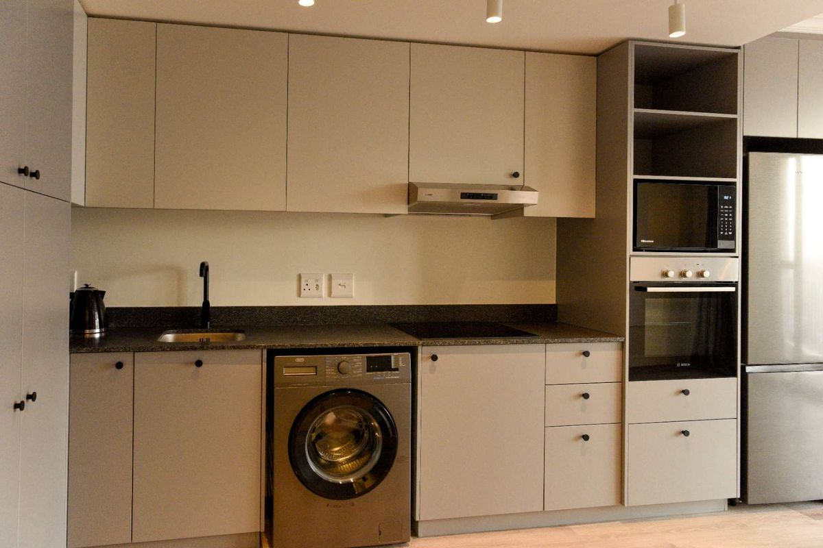Modern kitchen featuring sleek handleless cabinetry, stone countertops, integrated oven and microwave, electric hob, and a dedicated space for a washing machine.